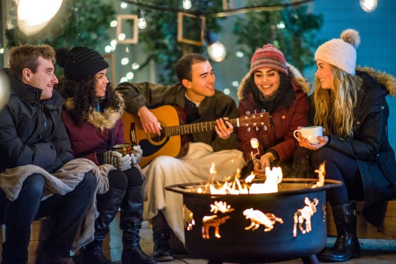 Fröhliche Menschen an Feuerschale im Winter